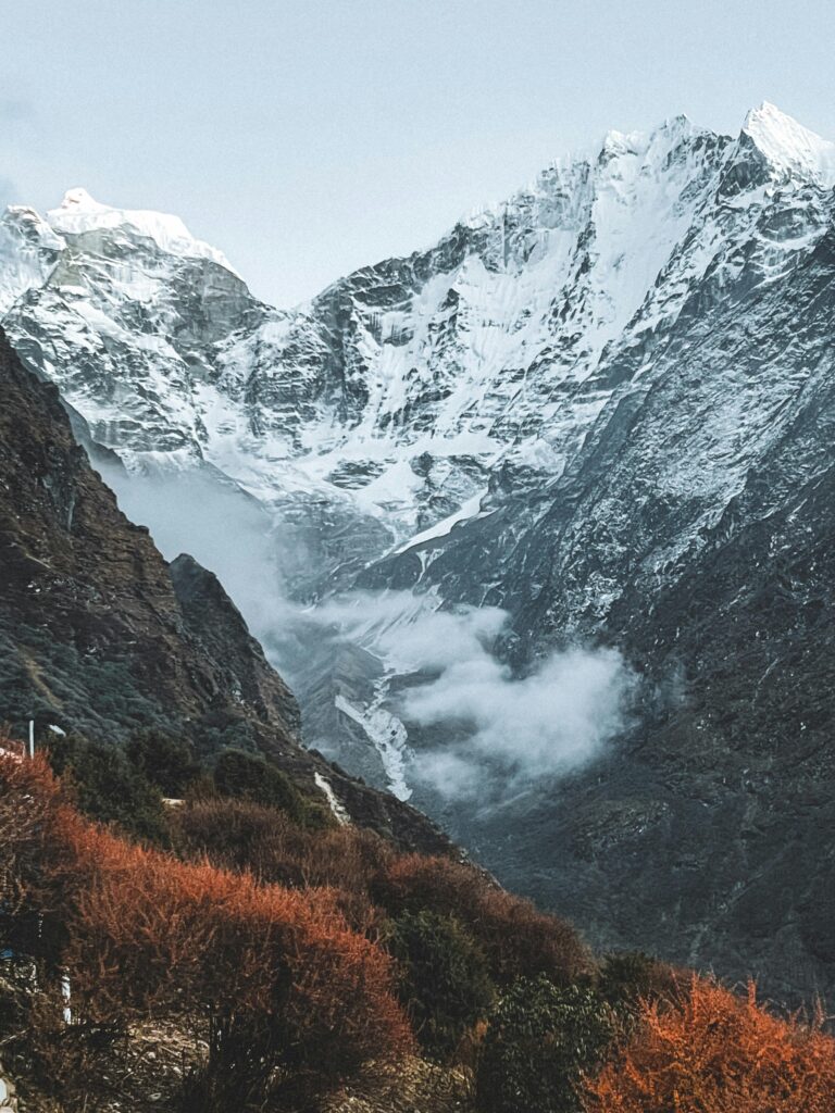 The snow-peaked himalayan mountains with some orange and green bushes at the bottom of the valley.