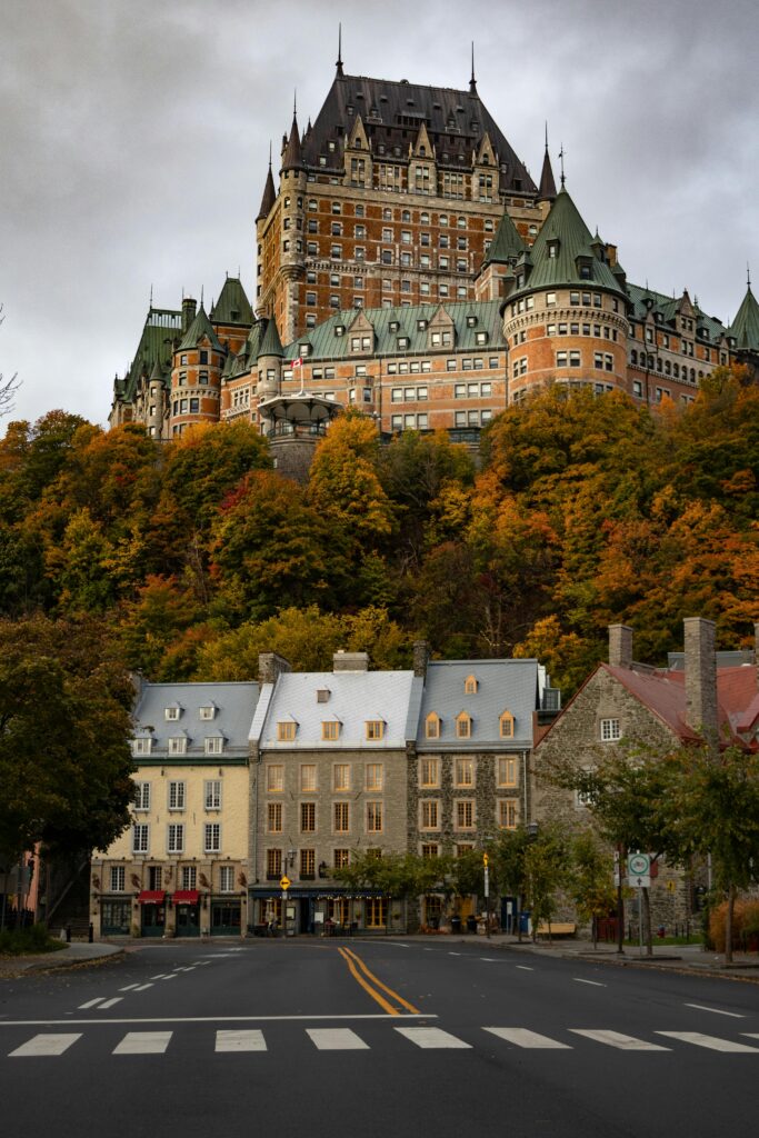 A view of the Fairmont Le Château Frontenac surrounded by a gloomy, cloudy sky in autumn, with green and orange trees over a street.