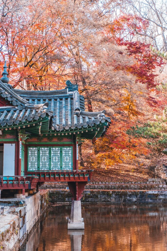 A jongmyo sitting atop a calm pond and surrounded by orange and brown leaves during an autumn day.